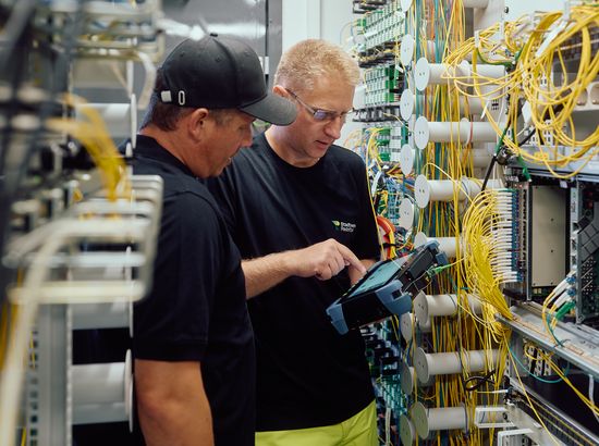 Zwei Techniker arbeiten an einer komplexen Netzwerk- oder Serverhardware mit vielen Kabeln und Anschlüssen. Sie führen Wartungs- oder Installationsarbeiten durch.