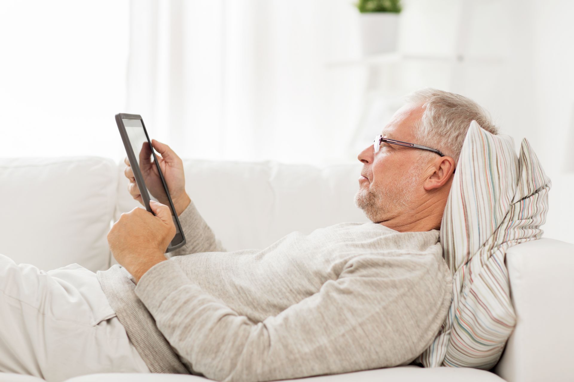 Ein älterer Mann liegt entspannt im Bett und hält ein Tablet in den Händen.
