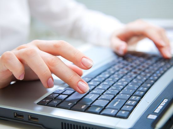 Person tippt auf die Tastatur eines Laptops mit beiden Händen.