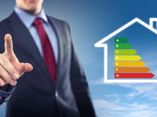 Ein Mann zeigt auf ein Haus mit Energieeffizienzlabel von A bis G, das verschiedene Energieeffizienzklassen darstellt.
