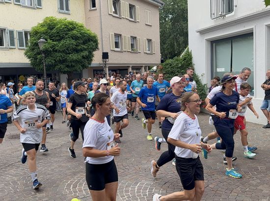Gruppe von Läufern nimmt an einem Straßenlauf teil, verschiedene Teilnehmer in Sportkleidung mit Nummern auf dem Rücken.