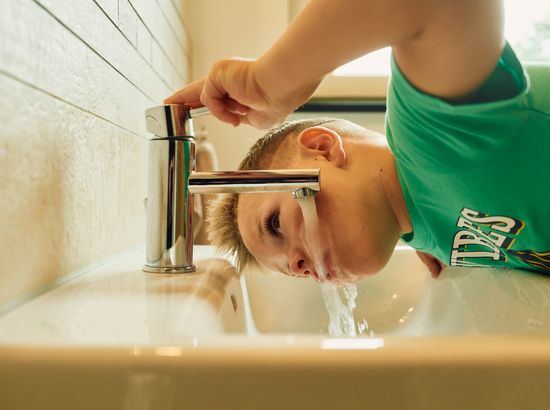 Ein Kind wäscht sich mit Wasser aus dem Hahn das Gesicht im Waschbecken.