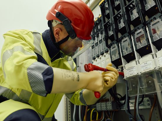 Ein Elektriker arbeitet an einer Verteileranlage und bedient mit beiden Händen einen Schalter oder eine Sicherung.