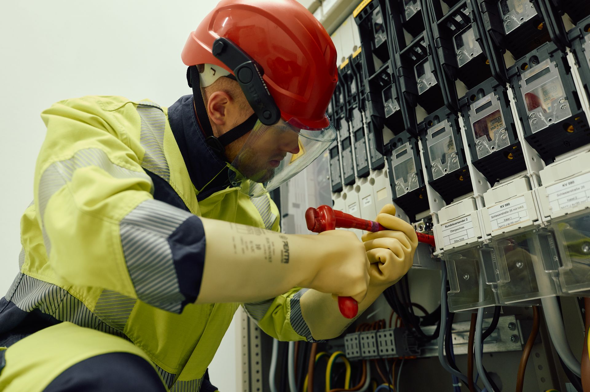 Ein Elektriker arbeitet an einer Verteileranlage und bedient mit beiden Händen einen Schalter oder eine Sicherung.
