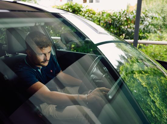 Ein Mann sitzt im Auto und hält ein Tablet, während er konzentriert auf den Bildschirm schaut.