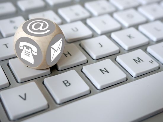 Ein Würfel mit den Symbolen für E Mail, Telefon und Brief liegt auf einer Computer-Tastatur.