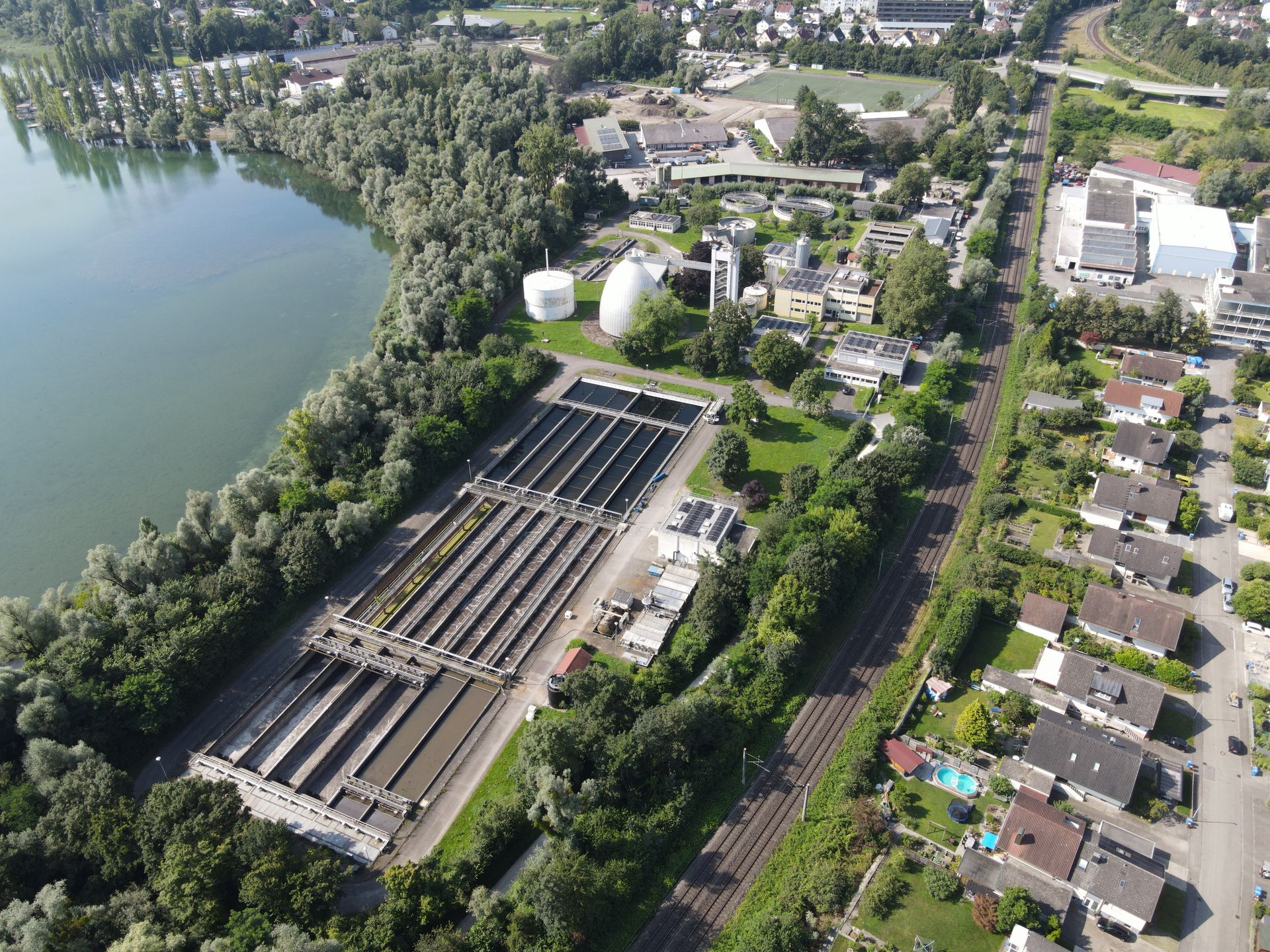 Luftbild einer Wasseraufbereitungsanlage mit Beckenreihen und Lagerbehältern am Ufer eines Sees.