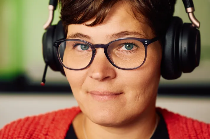 Eine Person mit Brille und Kopfhörern lächelt in die Kamera. Die Kopfhörer sind über den Ohren platziert.