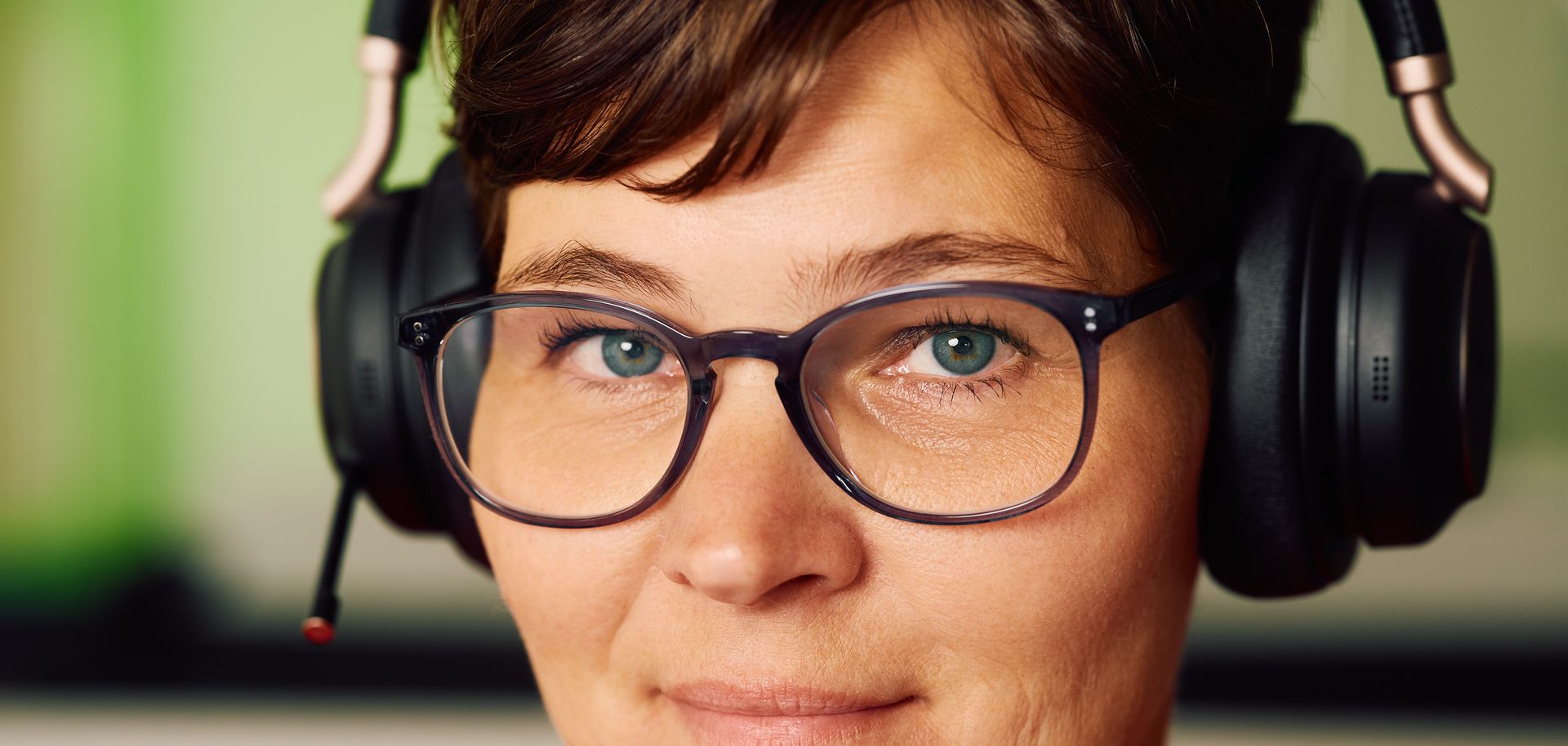 Eine Person mit Brille und Kopfhörern lächelt in die Kamera. Die Kopfhörer sind über den Ohren platziert.