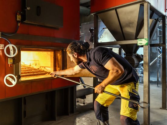 Ein Person bearbeitet im Glasofen mit einem Metallstab geschmolzenes Glas, um es zu formen.