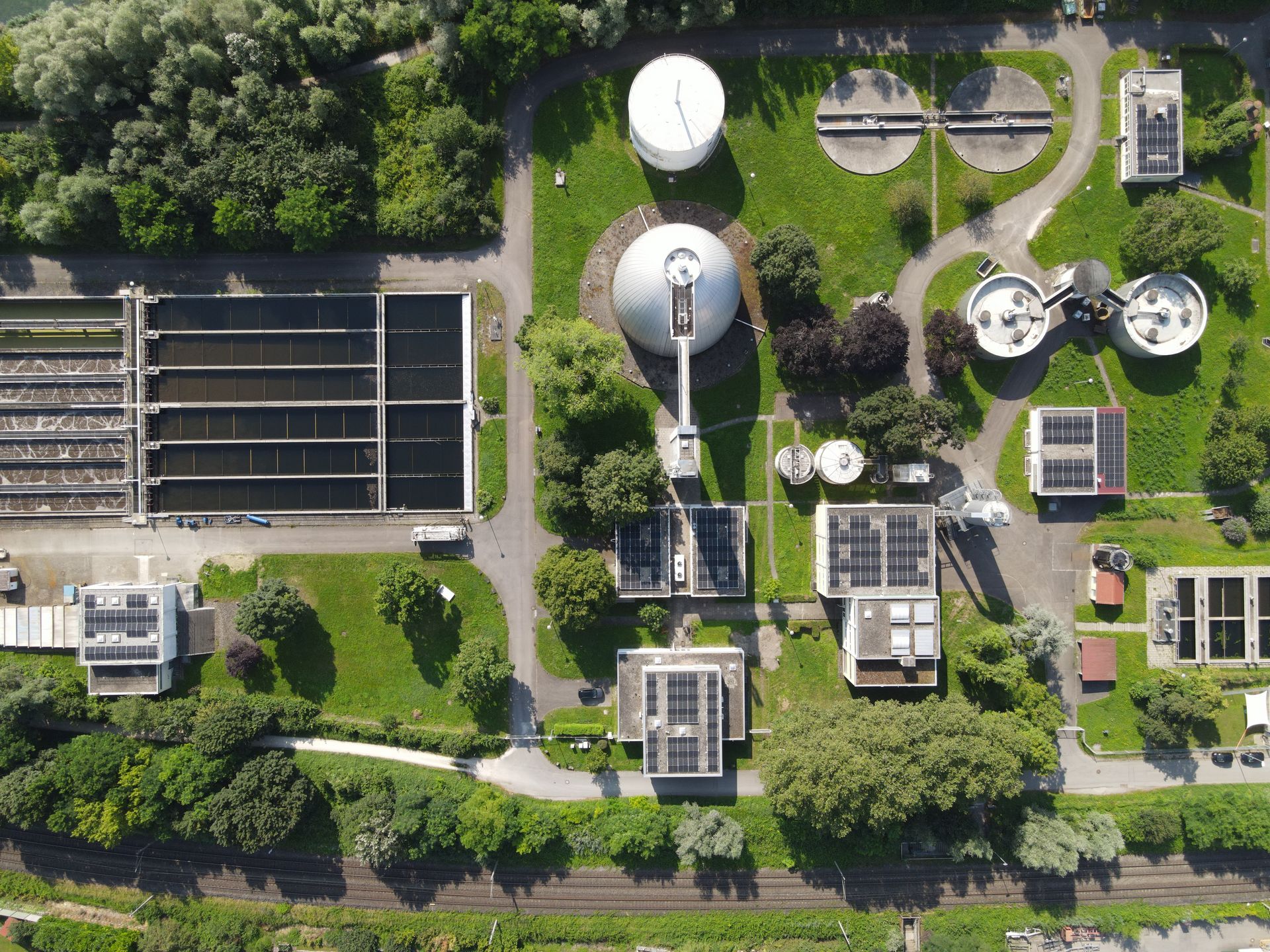 Aussicht von oben auf eine Industrieanlage mit mehreren großen Rundbehältern und technischen Gebäuden in einer grünen Umgebung.