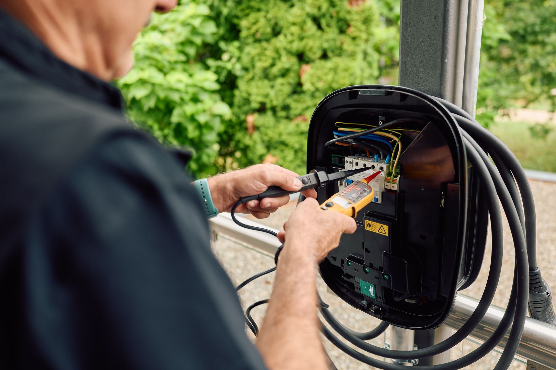 Ein Elektriker überprüft mit einem Messgerät die Verkabelung in einem offenen Elektroverteiler.