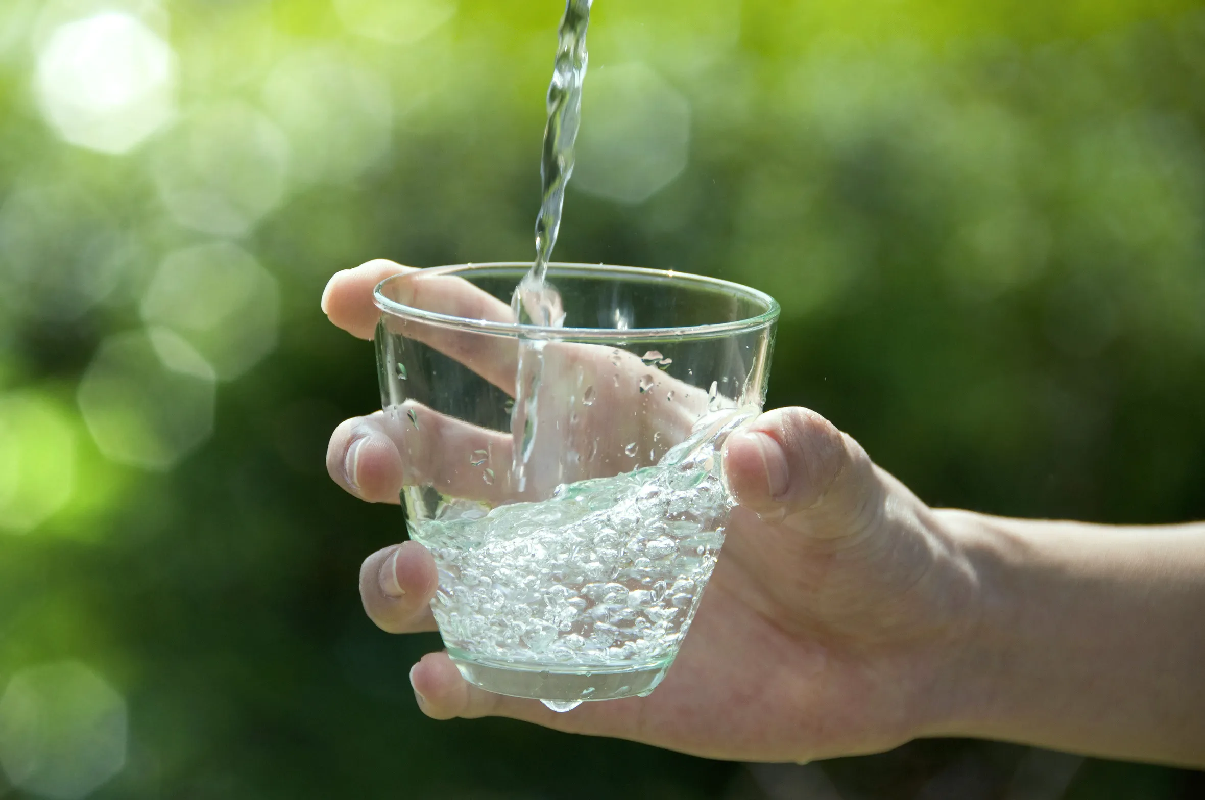 Ein Glas wird mit Wasser aus einer Quelle oder einem Behälter aufgefüllt.