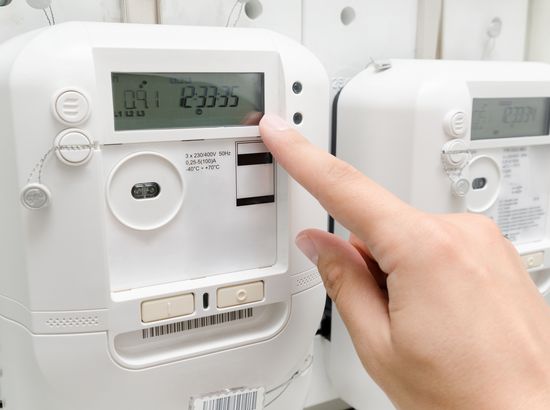 Eine Hand bedient die digitale Anzeige eines elektrischen Zählers mit der Zeit 2335. Der Zähler zeigt technische Daten und Messwerte an.