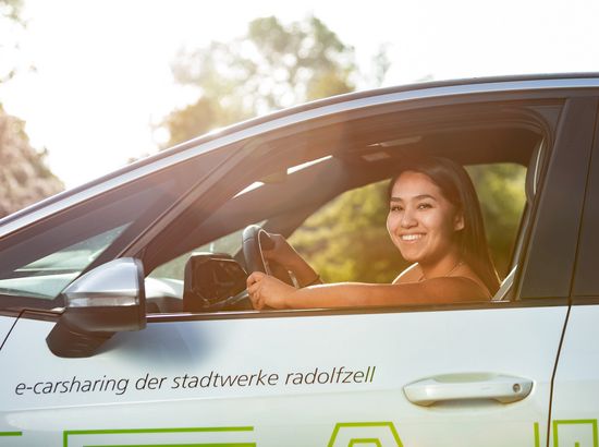 Eine Person sitzt lächelnd am Steuer eines E-Carsharing-Fahrzeugs der Stadtwerke Radolfzell und hält das Lenkrad.