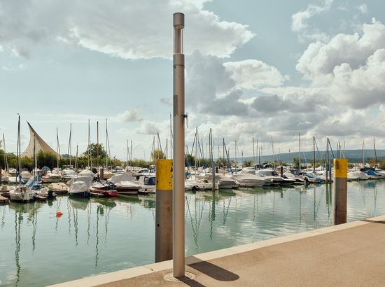 Marina mit zahlreichen Segelbooten und Yachten am Steg, ruhiges Wasser und Wolkenhimmel im Hintergrund.