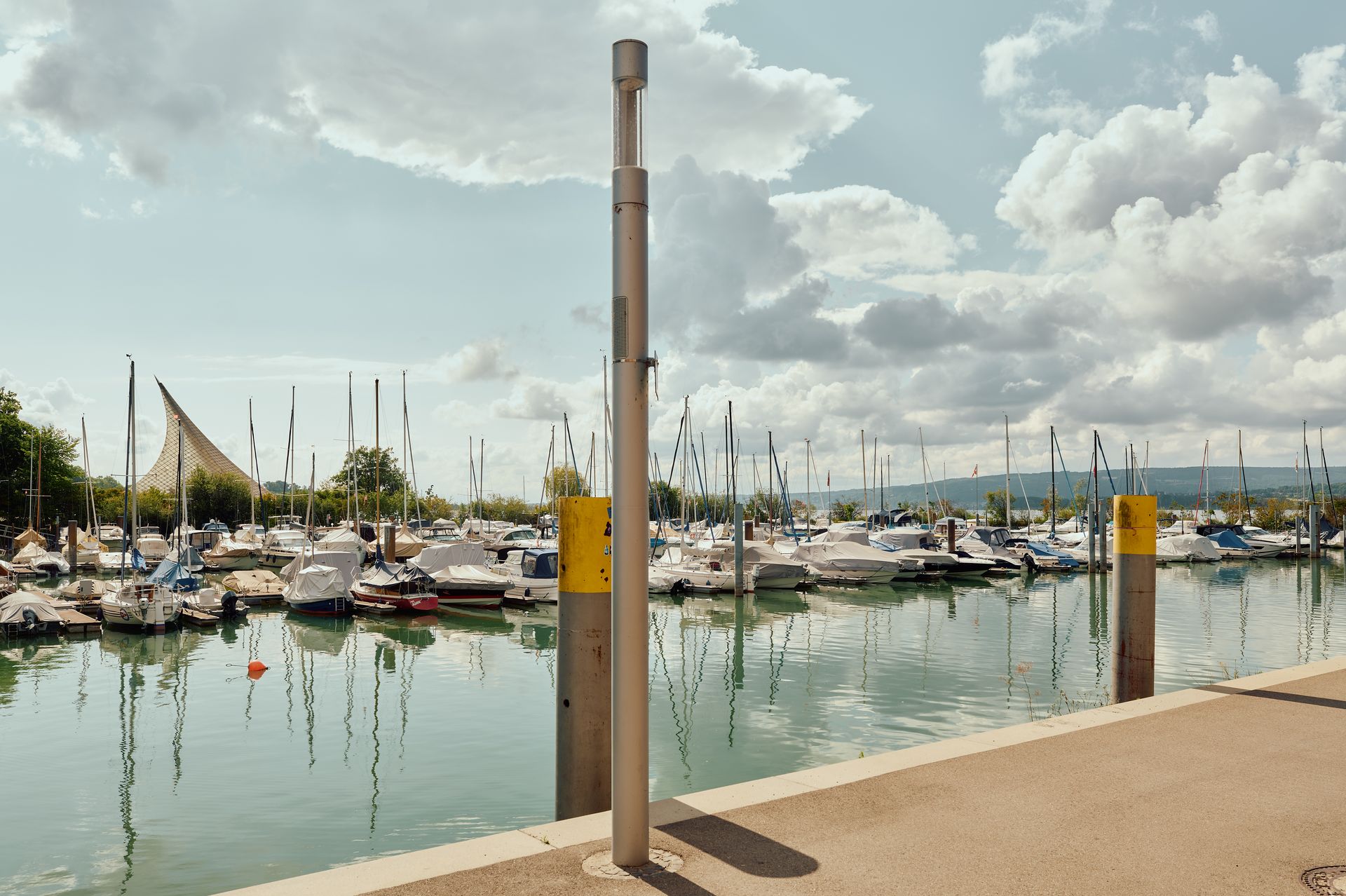 Marina mit zahlreichen Segelbooten und Yachten am Steg, ruhiges Wasser und Wolkenhimmel im Hintergrund.