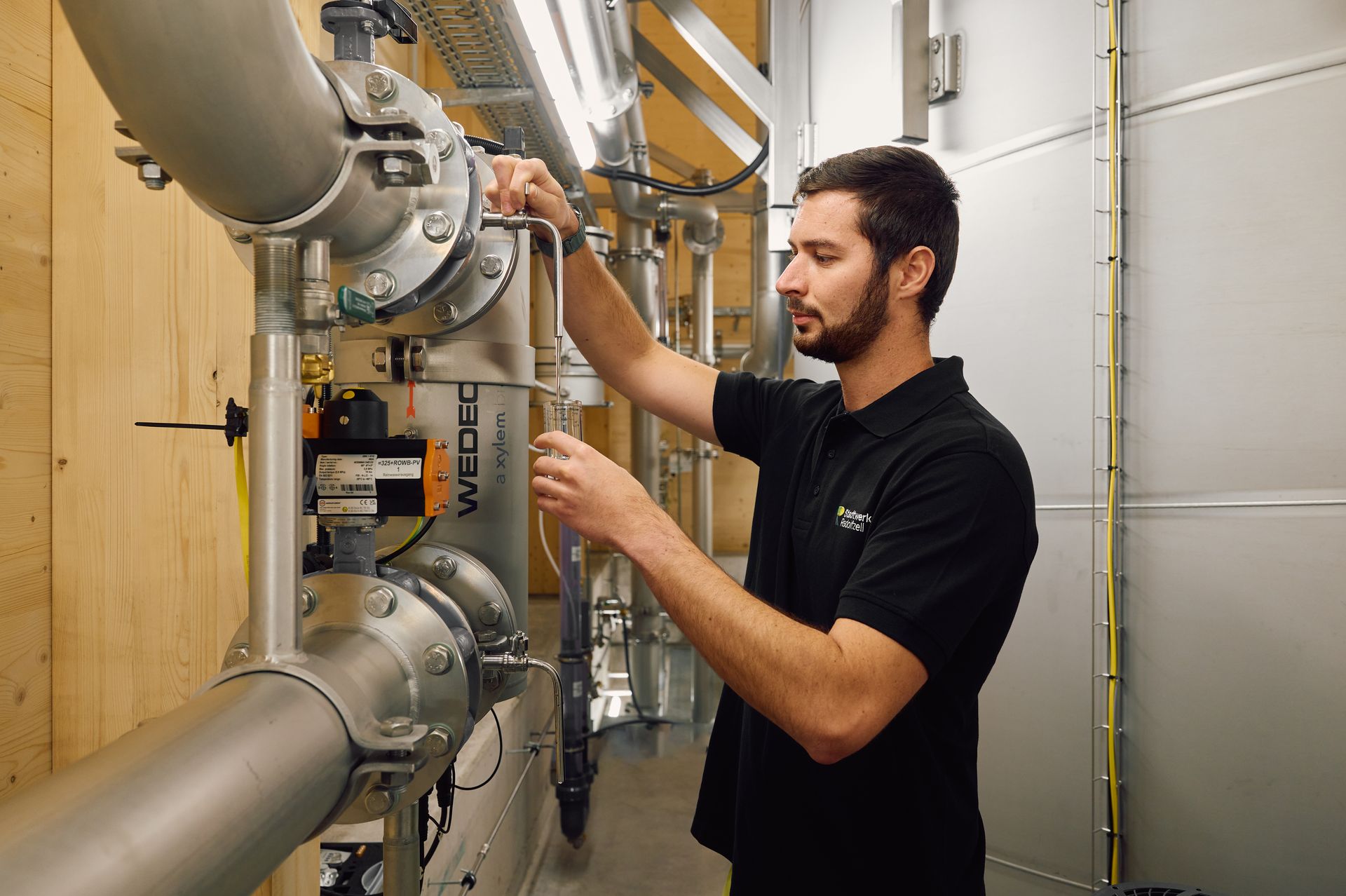 Ein Mitarbeiter entnimmt in einer Produktionshalle eine Probe aus einem Behälter der Brauerei oder Lebensmittelverarbeitung.