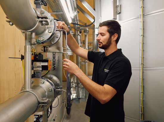 Ein Mitarbeiter entnimmt in einer Produktionshalle eine Probe aus einem Behälter der Brauerei oder Lebensmittelverarbeitung.