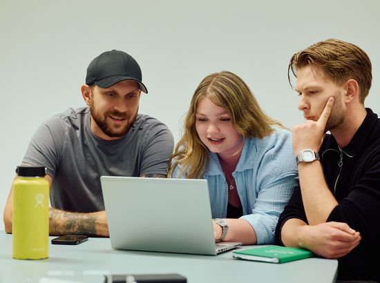 Drei Personen besprechen gemeinsam den Inhalt eines offenen Laptops an einem Tisch.